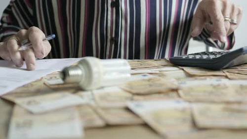 Close up shot desktop filled with 50 Euro bills, caucasian hands check calculator with and paper bil