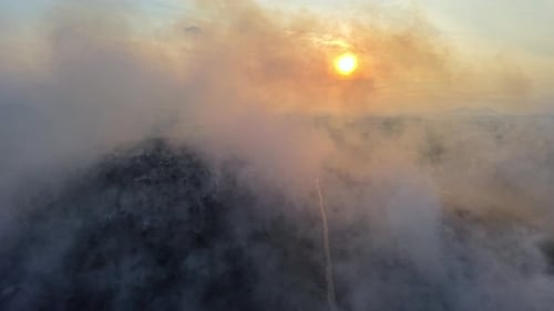 Smoke swirls around a sun setting over dark hills