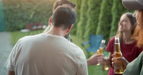 Une fille brune heureuse dans une casquette communique avec ses amis et boit des verres de bière pendant une soirée