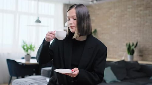 Young Woman Sitting at Home in Living Room Drinking Coffee