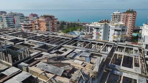 Vídeo aéreo de trabajadores en el último piso de un rascacielos ensamblando losas mientras el gancho de una grúa mueve materiales en