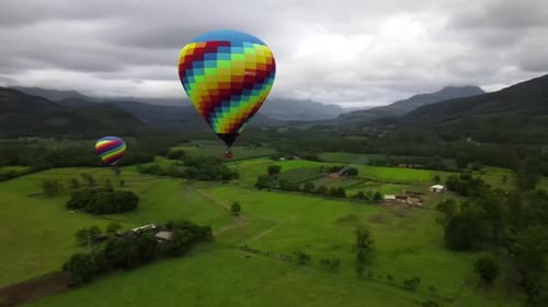 Orbital Aerial View of Colorful Hot Air Balloon Ride Flying at Dawn under a Cloudy Sky and a Small T