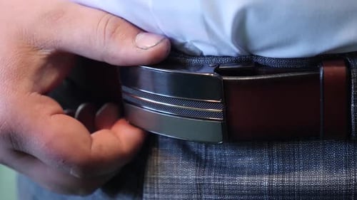 101. L'homme redresse et resserre la ceinture en cuir à l'aide d'une boucle en métal
.