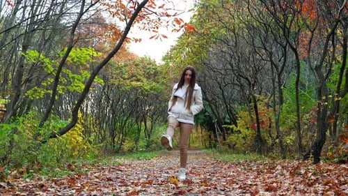 Attractive young woman walking down the park. Pretty lady walking by in autumn street.