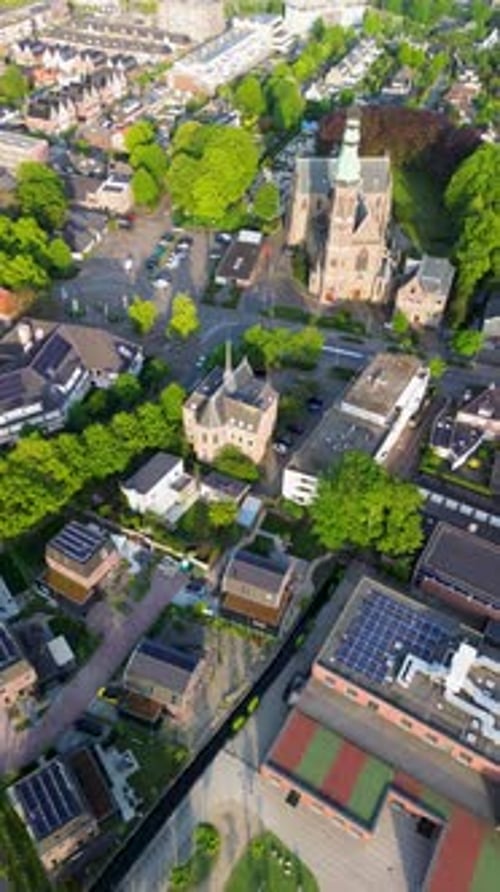 Aerial drone view of a town square with a parking lot, cars, trees, and geometric patterns