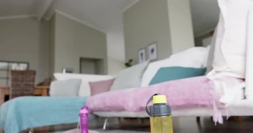 Close up of water bottles, towels and yoga mats on floor of living room, slow motion