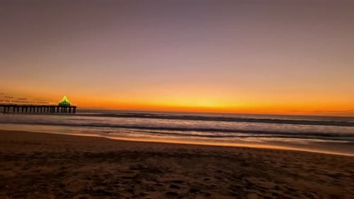 Vibrant sunset over a serene beach with a pier in the distance