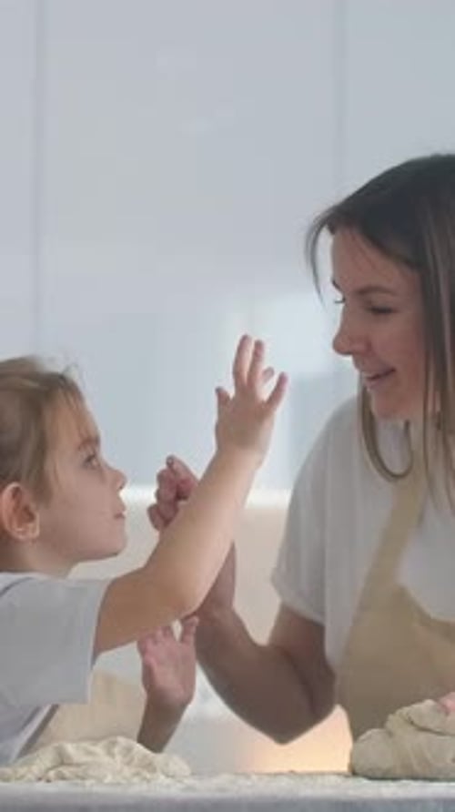 Smiling Mother and Young Daughter Happily Kneading Dough Together in a Bright Home Kitchen Sharing a