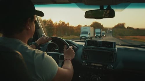 Person Steers the Car in Heavy Traffic on the Highway Full of Trucks During Sunset