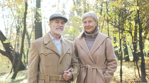 Portrait of Lovely Mature Husband and Wife Standing in Park in Autumn Looking at Camera Smiling