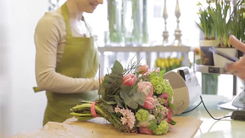 Happy florist woman counts bouquet cost as man pays with card at flower shop
