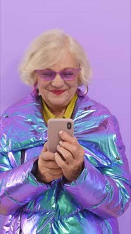 Une élégante femme âgée blonde utilise en toute confiance son smartphone pour montrer qu'elle est brillante et unique
