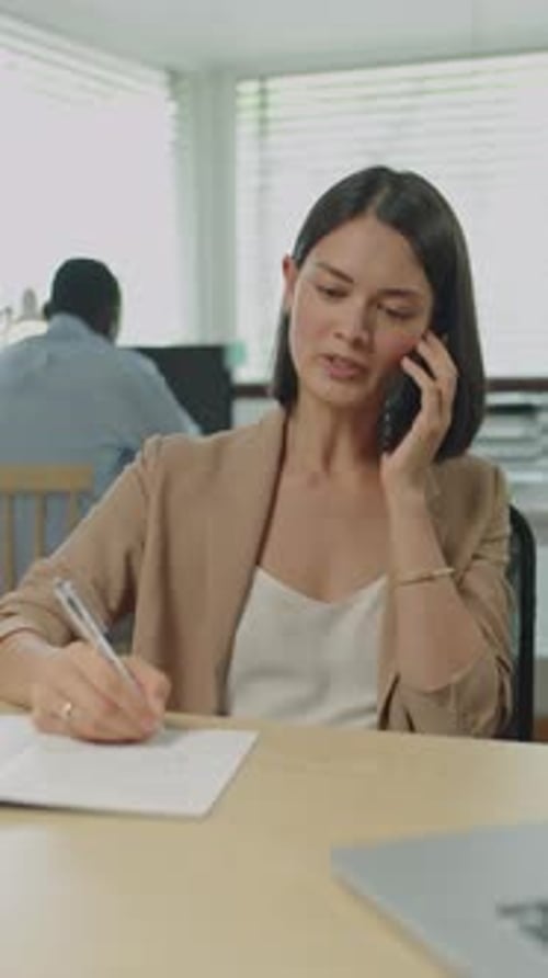 Female Office Worker Speaking on Phone and Making Notes