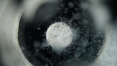 Imagen macro de una tableta blanca de aspirina soluble que burbujea en un vaso de agua sobre fondo oscuro