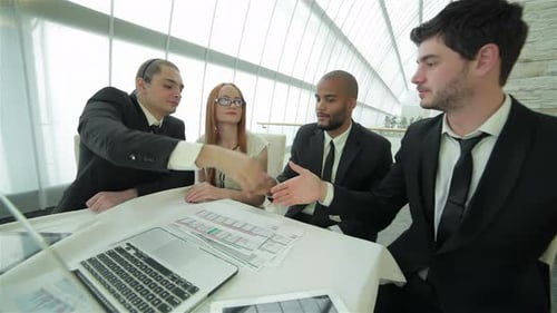 Four Smiling Successful Businessmen Sitting at Table in Office While Discussing