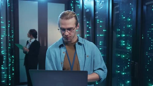 A Man Works in a Server Room Using a Laptop for Server Tasks