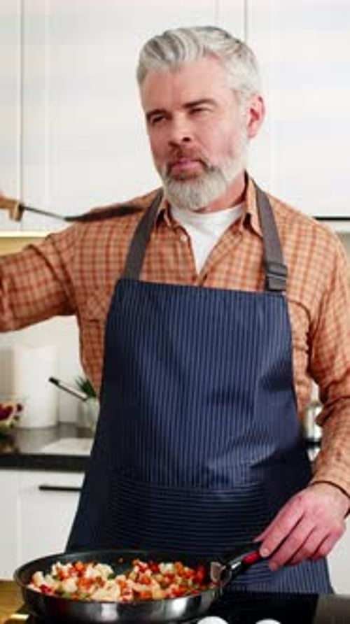Homem de meia idade temperando vegetais no fogão elétrico na cozinha de casa para uma refeição dietética saudável