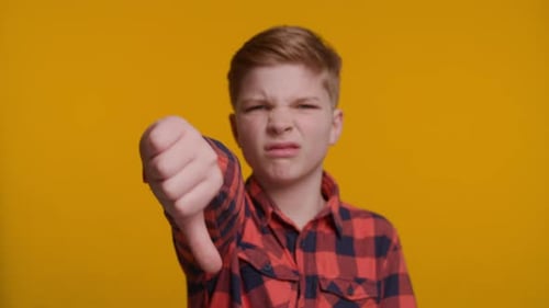 Boy Showing Thumbs Down at Camera on Yellow Background