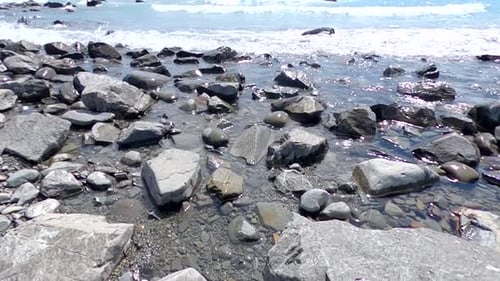 Nahaufnahme eines Seeufers mit Sichtweite von Steinen und Kieselsteinen unter Wasser und ruhigem Wellenplätschen