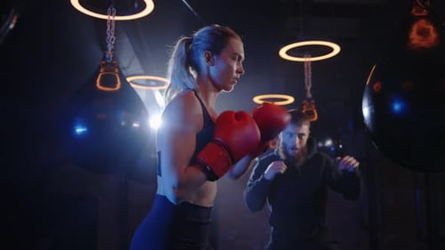 Woman Punching Heavy Bag in Gym with Trainer
