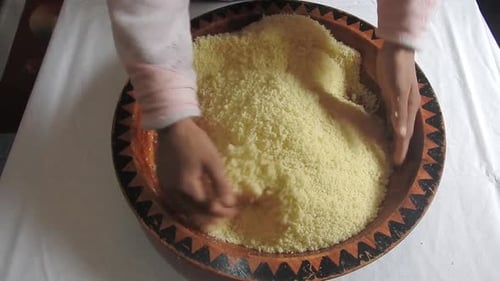 Frau rollt zu Hause heißen Couscous-Grieß zwischen ihren Finger in einer Holzschale, nachdem sie ihn gedämpft hat
