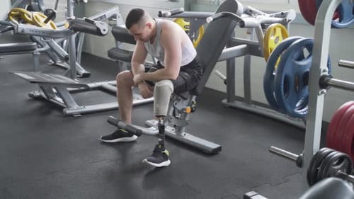 Man with prosthetic leg resting in the gym between sets during workout. Slow motion