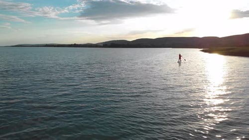 Aerial view of a woman paddle boarding on a SUP and enjoying relaxing vacation at amazing golden sun