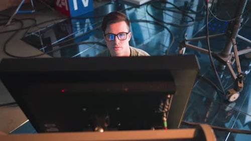 Person Working in TV Studio Wearing Glasses Focused on Computer Monitor