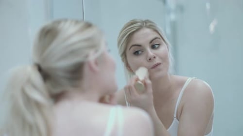 Woman applying makeup in a bright bathroom