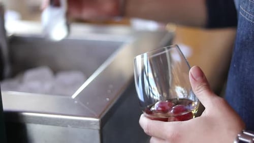 The person puts ice cubes in a glass of drink.