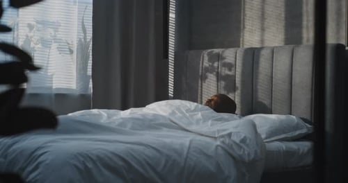 Im modernen, gemütlichen Schlafzimmer wacht der gutaussehende Mann im weißen Bett auf