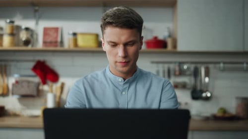 Junger Freelancer arbeitet remote von zu Hause aus in der Küche und tippt auf dem Laptop