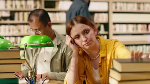Frustrated Young Woman Frowning at Laptop Between Tall Book Stacks
