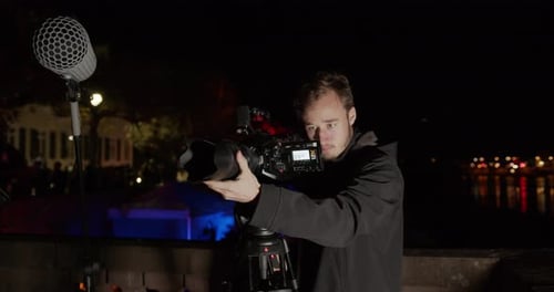 someone is filming a shoot with a cinema camera outside with a river in the background (Behind the S