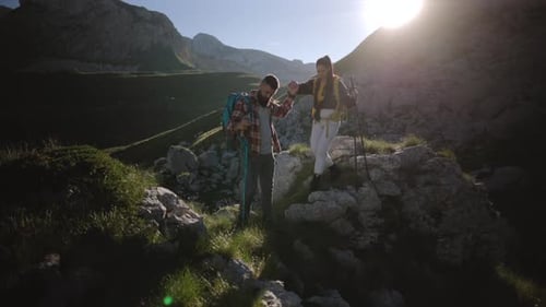 Young tourist couple hiking up scenic mountain trail during golden sunrise, experiencing breathtakin