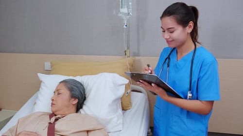 Asian nurse check saline and check patient elderly while asleep on bed at hospital ward.