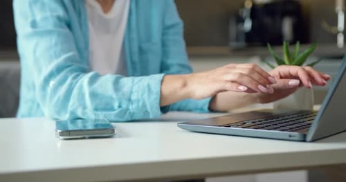 Nahaufnahme berühmter Hände einer unkenntlichen Frau am Tisch, die Computertastatur und Smartphone tippt