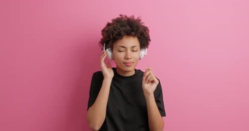 Woman with Headphones Dancing Against Pink Background