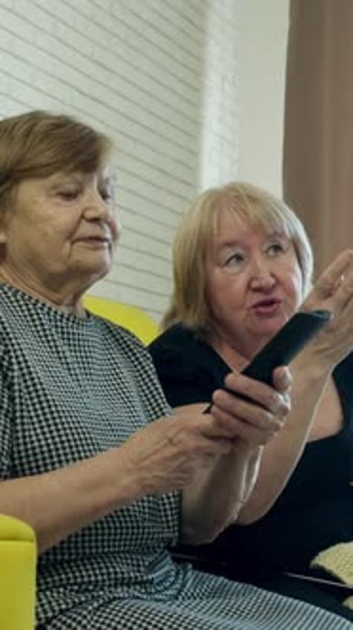 Two senior women watch television inside their home