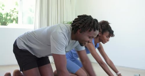Pareja chocando los cinco para comenzar el entrenamiento arrodillada en casa sobre colchonetas verdes, bajando para hacer flexiones