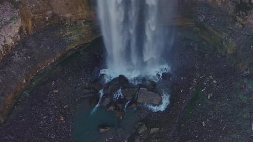 A waterfall cascading into a rocky pool in a serene forest setting, aerial view