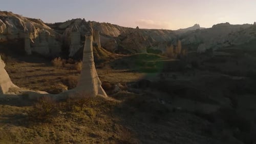 Vol de drone entre des formations rocheuses inhabituelles allongées ressemblant à des cheminées ou à des phallus, illuminées