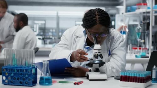 Scientist Using Microscope and Taking Notes in Lab