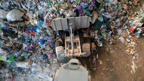 Drone view of an excavator picking up garbage from a huge heap of plastic garbage at waste sorting p