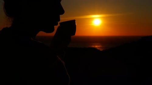 Silhouette of a Woman Drinking Coffee at Sunrise Over the Ocean