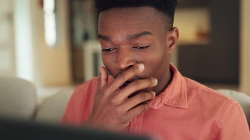 Tired, burnout and african man on a laptop working on a project while sitting on a sofa