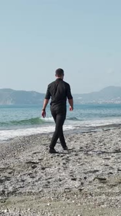 Vertikales Video Mediterrane Gelassenheit Ein Mann in Schwarz macht einen entspannenden Küstenspaziergang