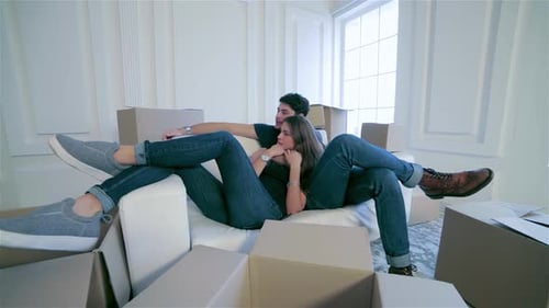 Joyful Couple in Love Relaxing on a Sofa Surrounded By Moving Boxes