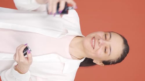 Woman Sprays Perfume on Hair Against Orange Background