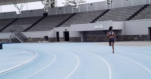 A woman runner or athlete running along a race track at a stadium for sport and fitness